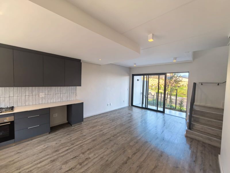 Modern open-plan living area featuring a sleek kitchen with dark cabinetry, integrated appliances, laminate flooring, and sliding doors leading to an outdoor space.