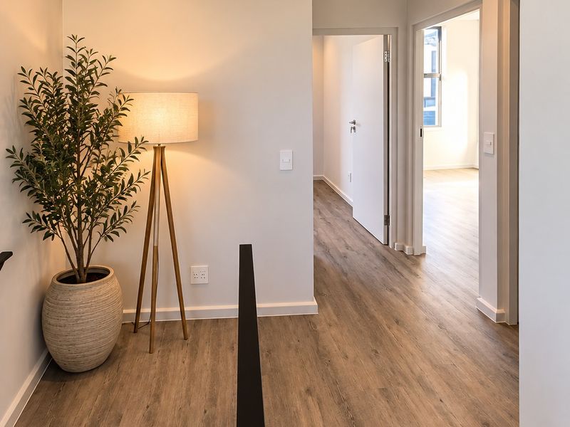 A bright and modern hallway featuring wood-look laminate flooring, recessed downlighting, and clean neutral walls leading to adjacent rooms.