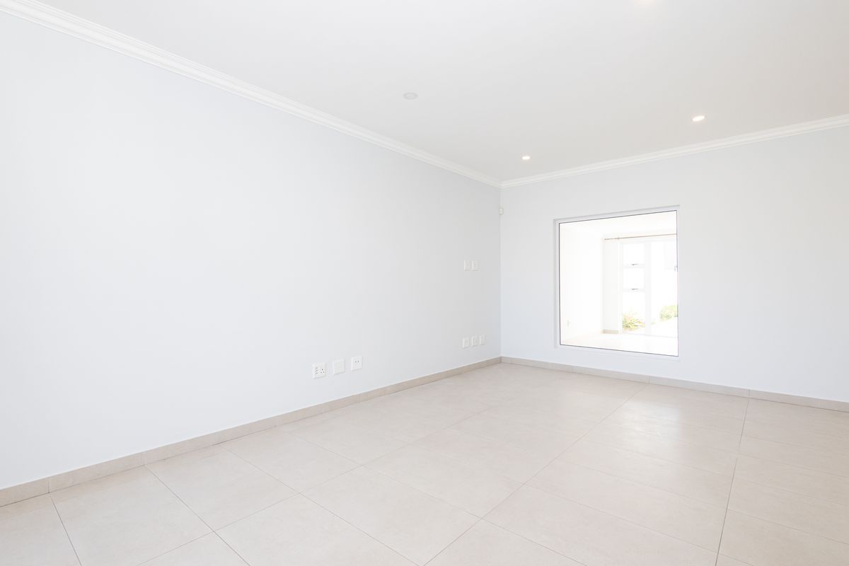A bright, empty living room featuring neutral tiled flooring, recessed downlighting, and clean white walls, offering a versatile space ready for furnishing.