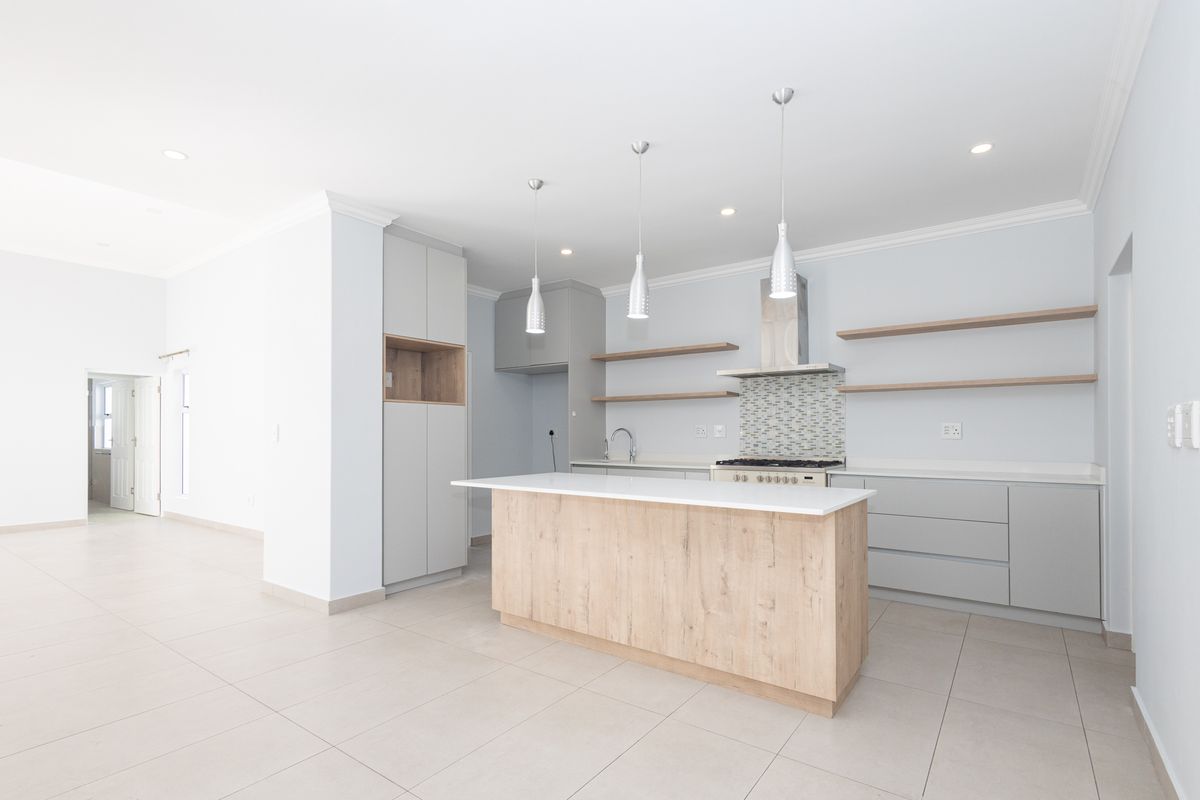 Modern open-plan kitchen featuring a central island, light wood cabinetry, gas hob, extractor fan, and sleek tiled flooring.