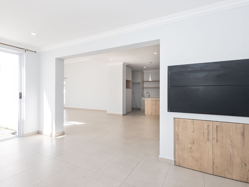 Spacious open-plan living area featuring neutral tiled flooring, modern built-in cabinetry, and seamless access to the outdoor patio through a sliding glass door.