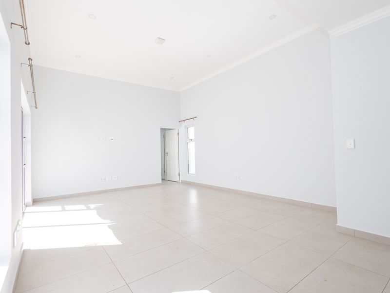 A bright, spacious, and empty living area featuring neutral tiled flooring, recessed lighting, and clean white walls, ready for personalization.