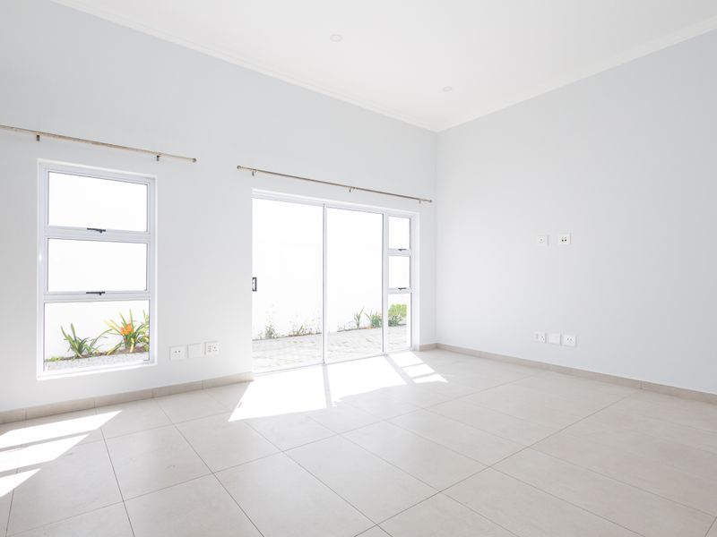 A bright, empty living room featuring neutral tiled flooring, large sliding glass doors, and aluminium windows, offering a clean and versatile space.