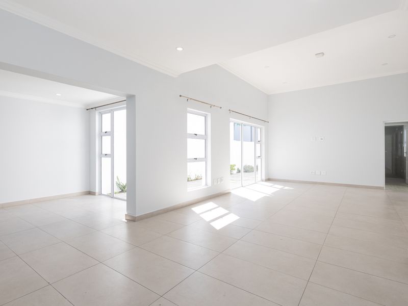 A bright and spacious open-plan living area featuring neutral tiled flooring, recessed lighting, and multiple glass doors providing ample natural light.