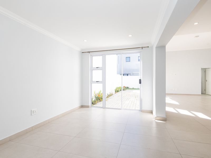 Bright and spacious open-plan living area featuring neutral tiled flooring, recessed lighting, and a sliding glass door providing access to the rear patio.