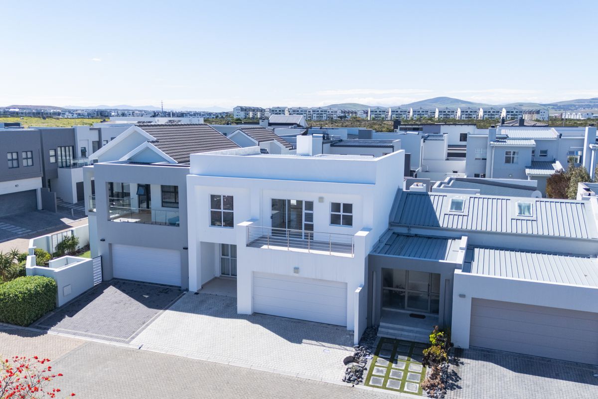 Aerial view of a modern residential property featuring a double garage, paved driveway, and upper-level balcony in a well-maintained estate setting.