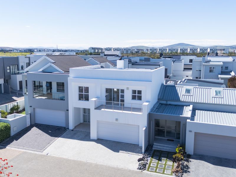 Aerial view of a modern residential property featuring a double garage, paved driveway, and upper-level balcony in a well-maintained estate setting.