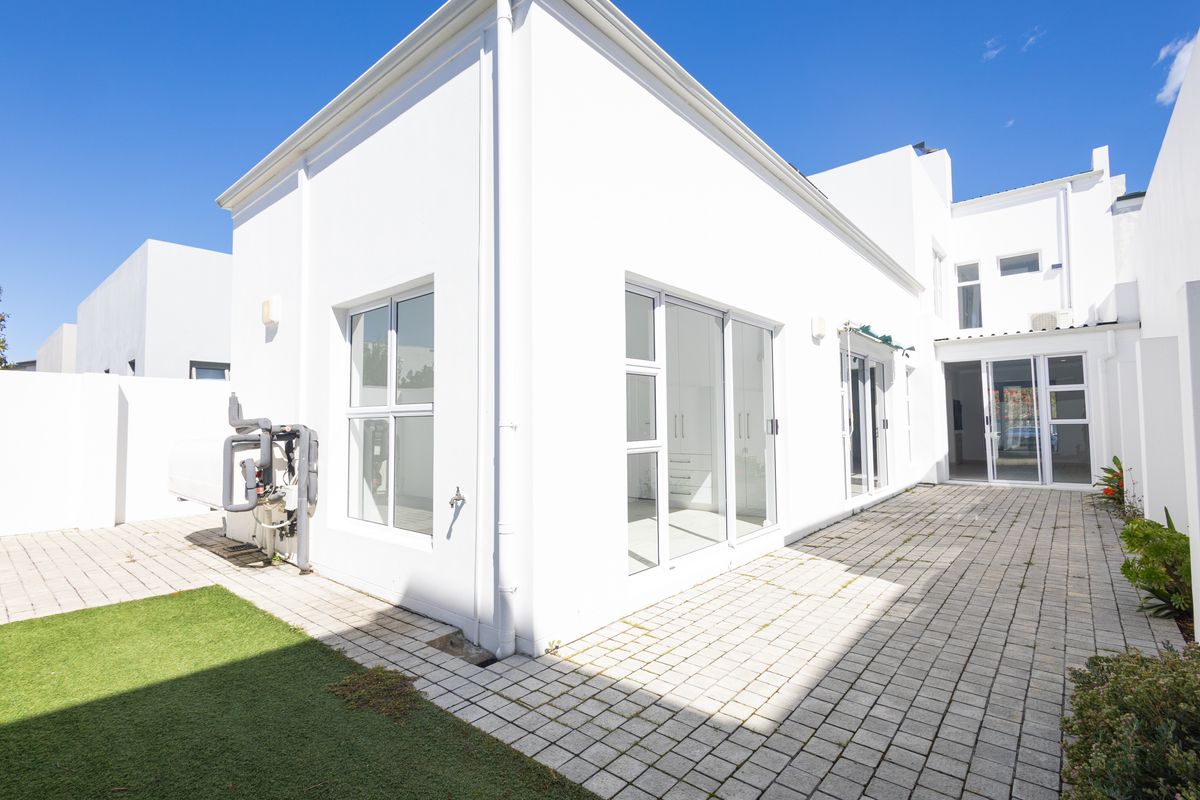 Rear exterior view featuring a paved patio area, sliding glass doors, and low-maintenance artificial lawn.