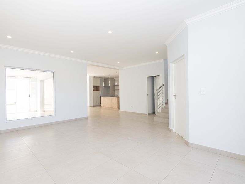 Spacious open-plan living area featuring neutral tiled flooring, recessed lighting, and a seamless transition to a modern kitchen and staircase.