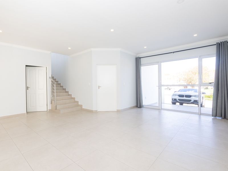 A bright, open-plan living area featuring neutral tiled flooring, recessed lighting, and large sliding glass doors providing natural light and access to the exterior.