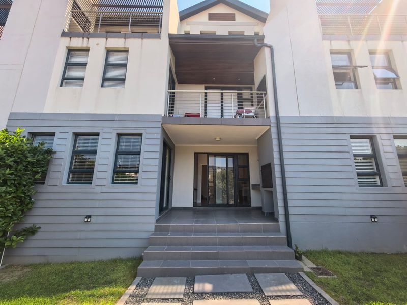 Front elevation of a multi-story apartment building featuring tiled entrance steps, a balcony with stainless steel railings, and modern aluminium window frames.