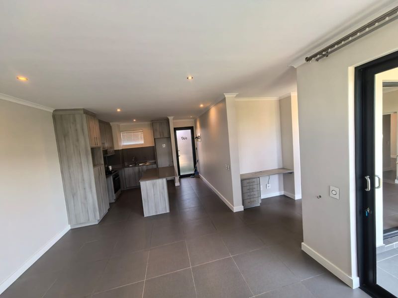 Modern open-plan living area featuring a contemporary kitchen with built-in cabinetry, a central island, and a dedicated built-in desk space with tiled flooring throughout.