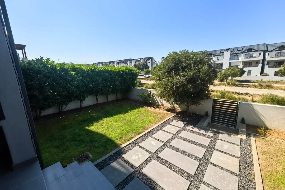 A private rear garden featuring a manicured lawn, paved pathway, and secure boundary wall with a metal gate.