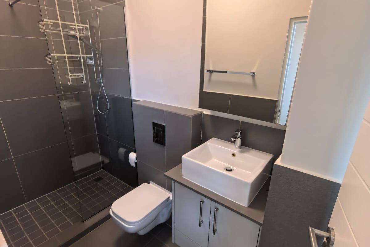 Modern bathroom featuring a walk-in shower with glass screen, wall-mounted toilet, and a vanity unit with a vessel sink.