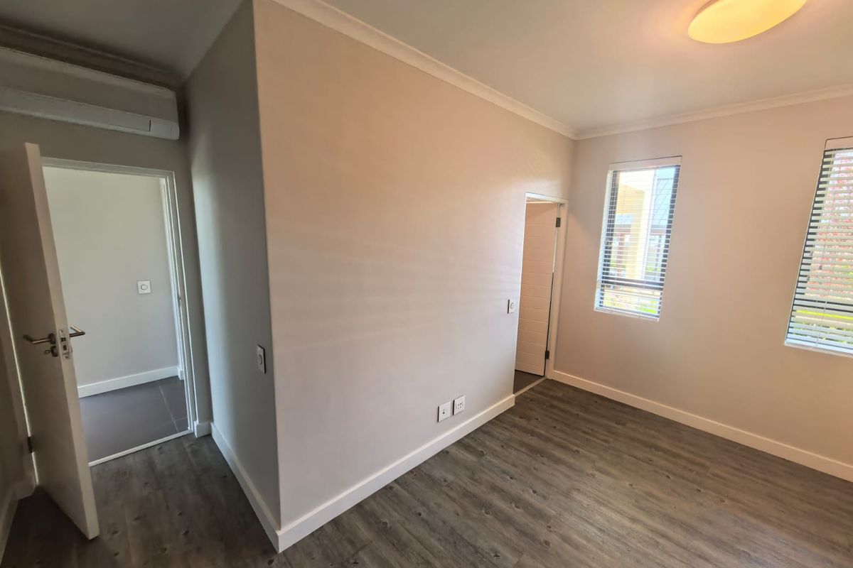 A bright, empty bedroom featuring modern laminate flooring, air conditioning, and venetian blinds, offering a clean and neutral space ready for personalization.