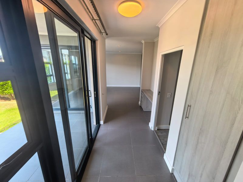 A bright, modern hallway featuring large sliding glass doors, neutral tiled flooring, and built-in storage cabinetry, leading into an open-plan living area.
