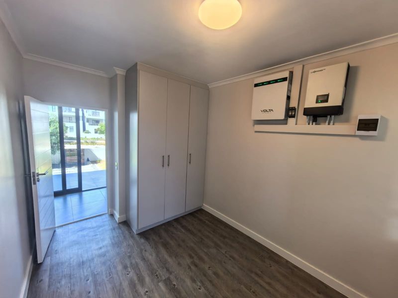 A clean utility room featuring built-in cupboards and a modern solar power installation, including an inverter and battery system, with direct access to the patio.