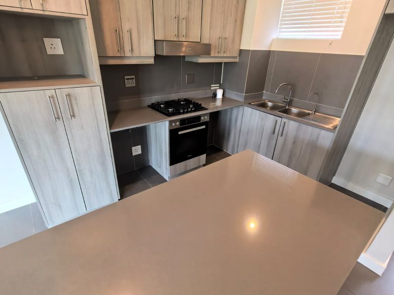 Modern kitchen featuring light wood-grain cabinetry, stone countertops, a gas hob, built-in oven, and a double bowl sink with tiled splashback.