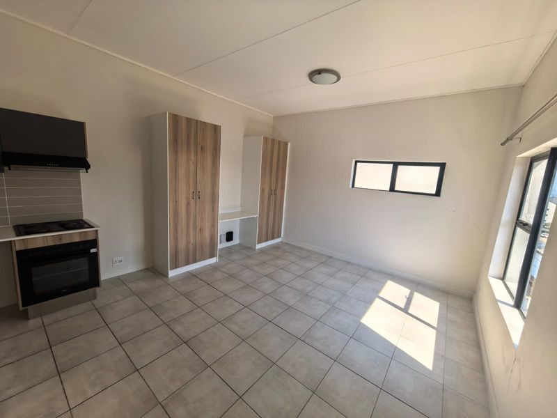 An open-plan living and kitchen area featuring tiled floors, built-in cabinetry, a built-in oven with hob, and a small integrated desk space.