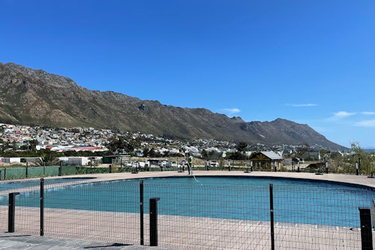A well-maintained outdoor swimming pool area featuring a paved deck, perimeter fencing, and scenic mountain views in the background.