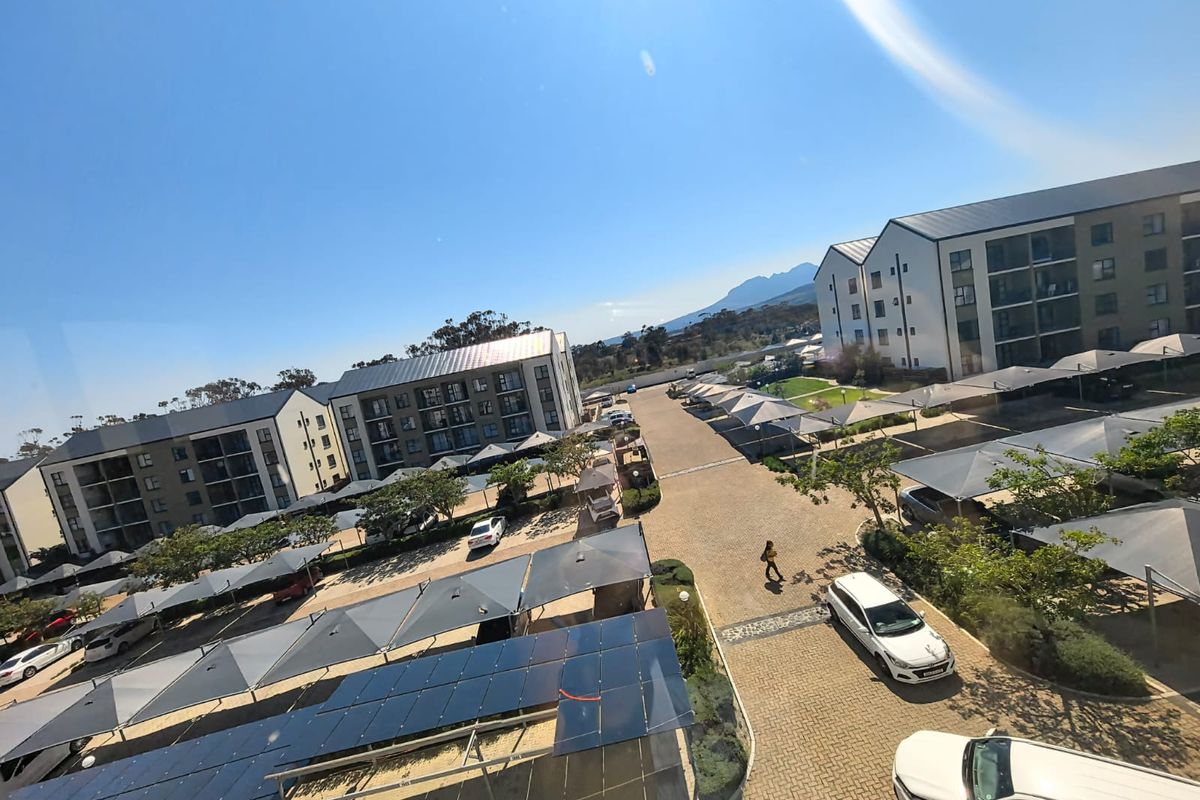 An elevated aerial view of the apartment complex grounds, featuring paved driveways, covered parking structures, and a large solar panel installation.