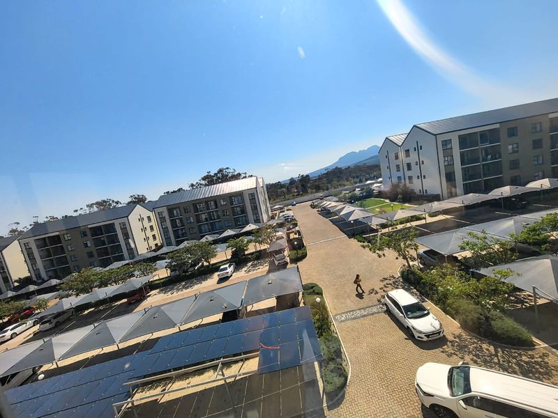An elevated aerial view of the apartment complex grounds, featuring paved driveways, covered parking structures, and a large solar panel installation.