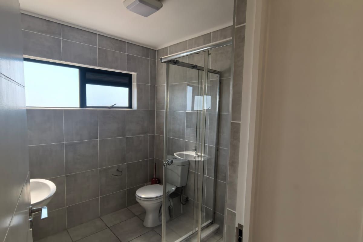 A clean, modern bathroom featuring grey wall and floor tiles, a glass shower enclosure, a toilet, and a wall-mounted basin.