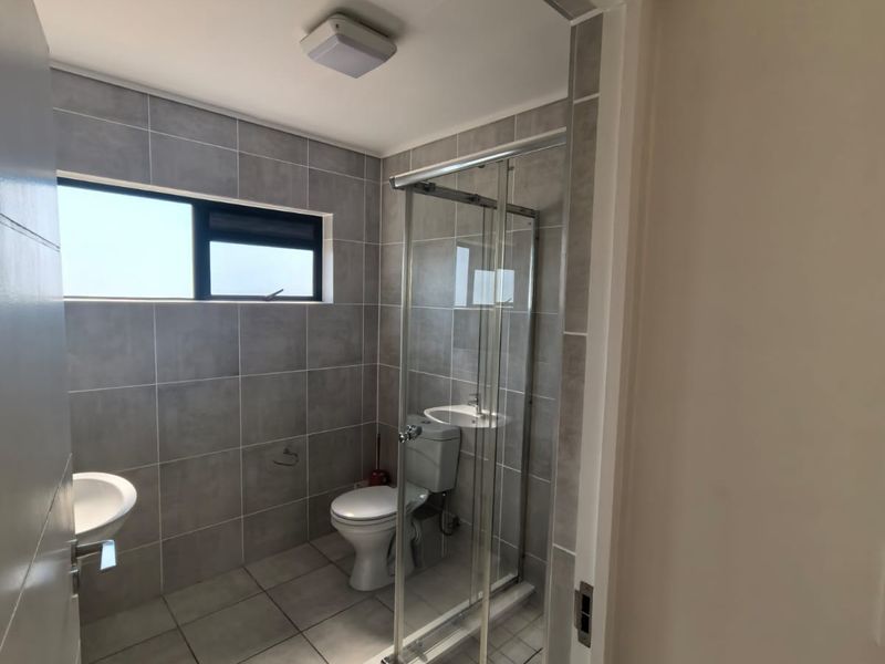 A clean, modern bathroom featuring grey wall and floor tiles, a glass shower enclosure, a toilet, and a wall-mounted basin.