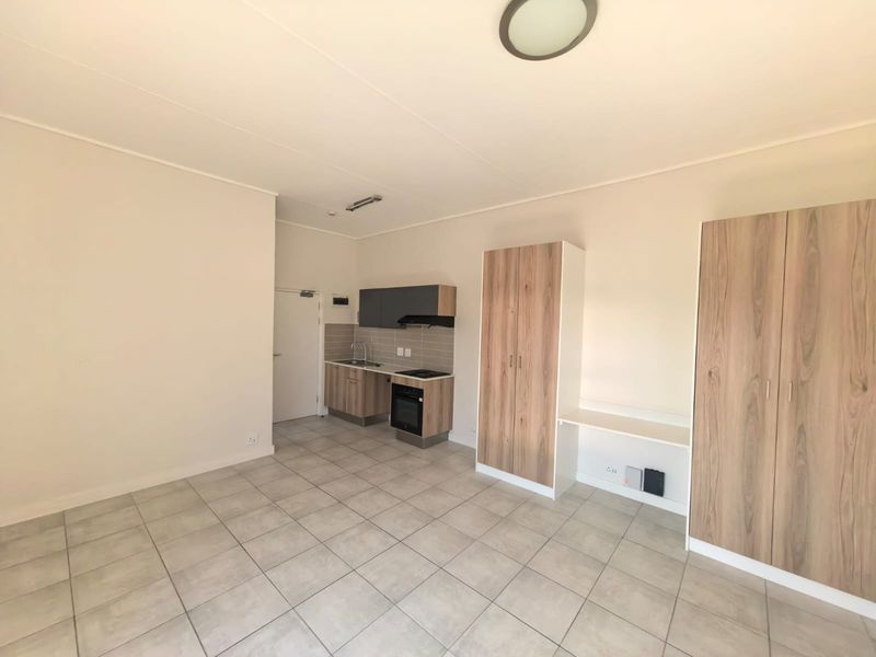 Open-plan living area featuring a compact kitchen with built-in appliances, tiled flooring, and integrated storage cupboards.
