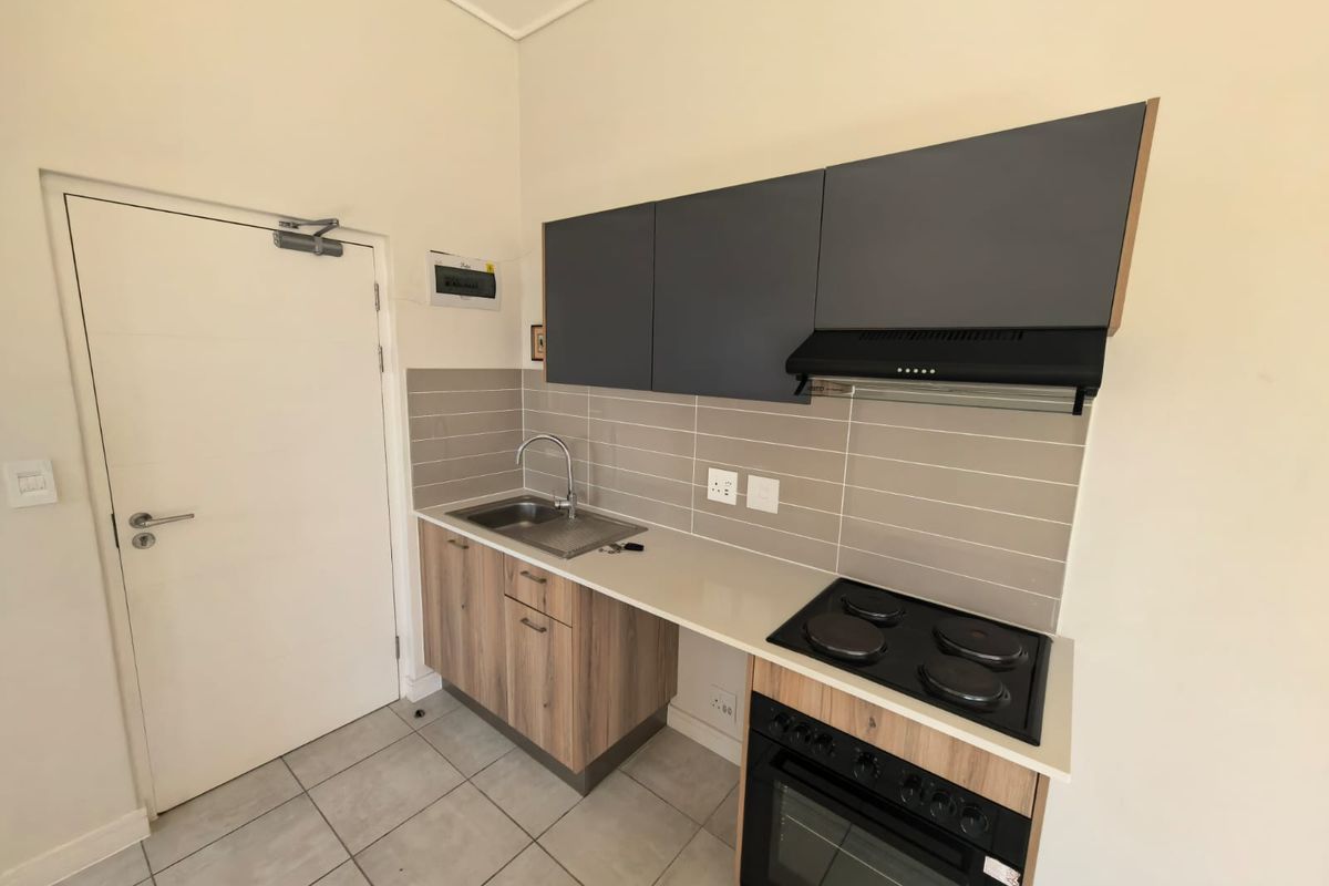 Compact modern kitchen featuring wood-finish lower cabinets, dark grey upper cupboards, integrated electric oven and hob, and a tiled backsplash.