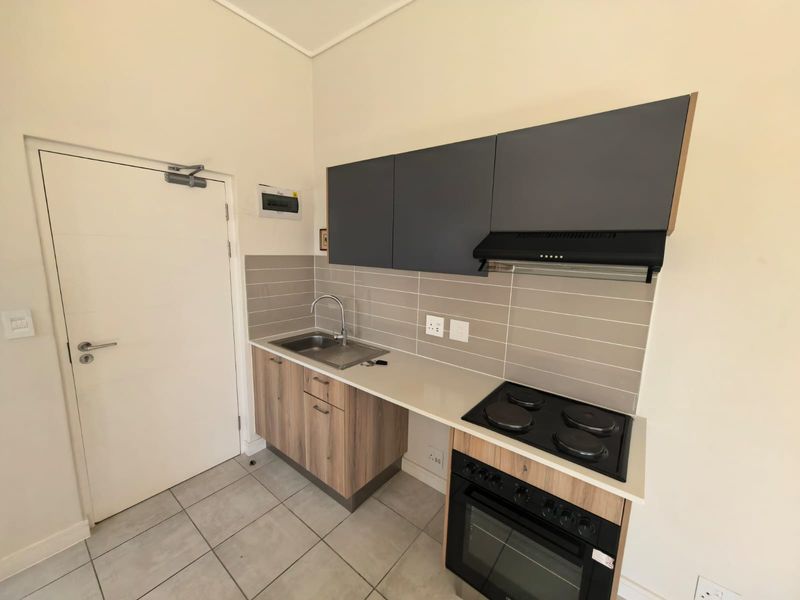 Compact modern kitchen featuring wood-finish lower cabinets, dark grey upper cupboards, integrated electric oven and hob, and a tiled backsplash.