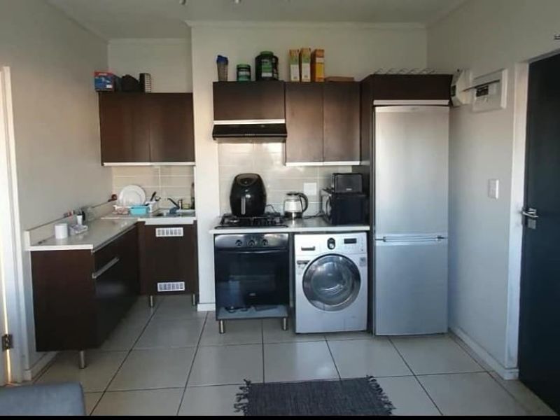 Compact open-plan kitchen featuring dark wood cabinetry, tiled flooring, and integrated appliances, seamlessly connected to the living area.