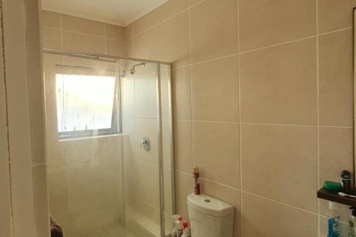 A functional bathroom featuring a glass-enclosed shower, a standard toilet, and neutral wall tiling throughout.