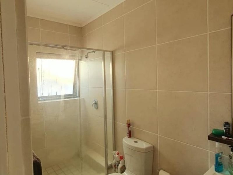 A functional bathroom featuring a glass-enclosed shower, a standard toilet, and neutral wall tiling throughout.