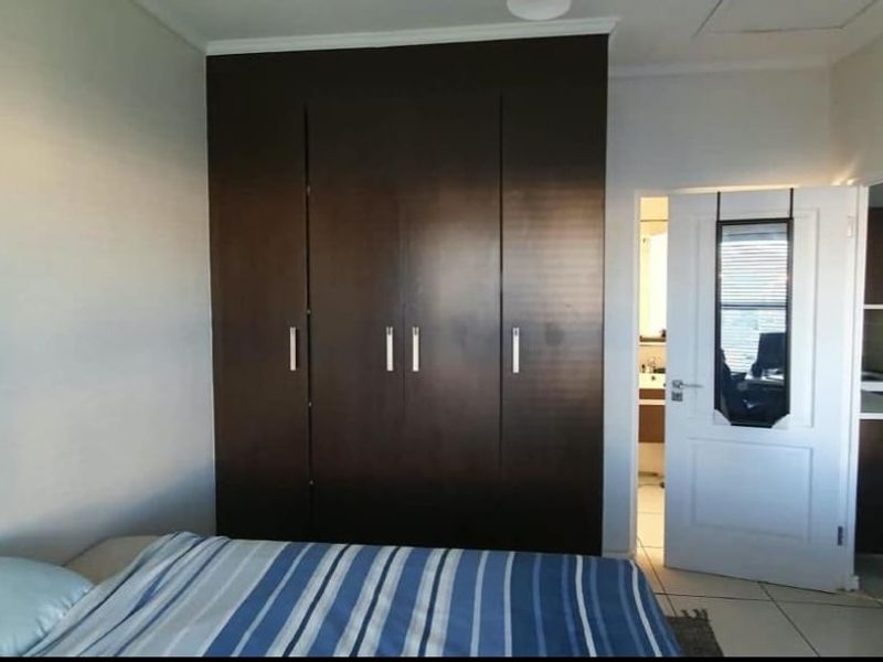 A bedroom featuring dark wood built-in cupboards and tiled flooring, with an adjacent view into a bathroom and kitchen area.