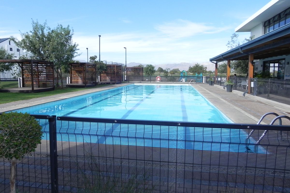 A well-maintained communal swimming pool area featuring a lap pool, safety fencing, and shaded timber pergolas set within a landscaped estate environment.