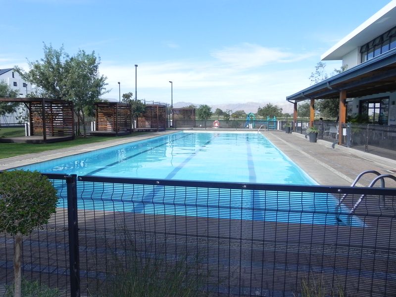 A well-maintained communal swimming pool area featuring a lap pool, safety fencing, and shaded timber pergolas set within a landscaped estate environment.