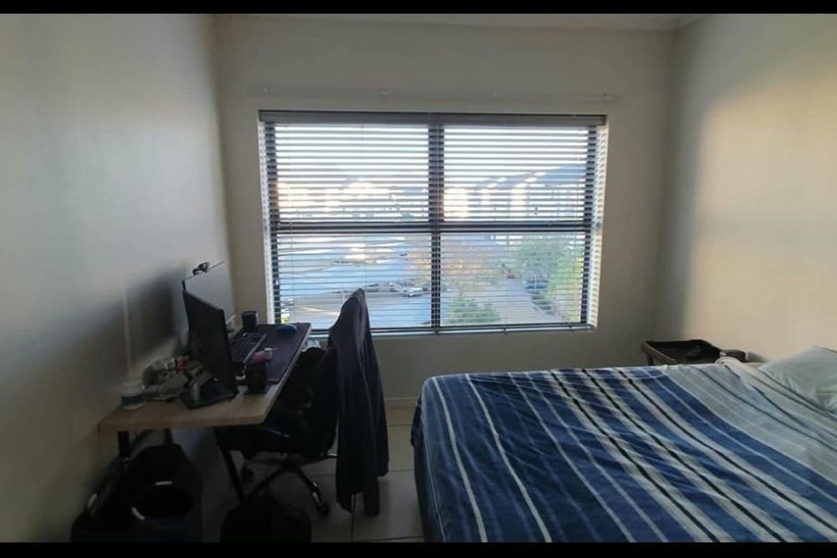 A functional bedroom featuring tiled flooring and a large window with fitted blinds, offering natural light and a view of the surrounding area.
