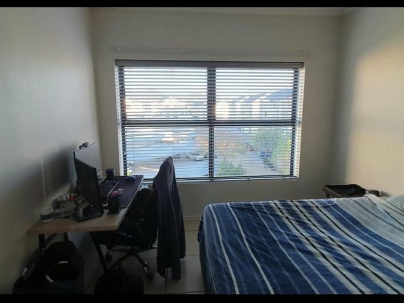 A functional bedroom featuring tiled flooring and a large window with fitted blinds, offering natural light and a view of the surrounding area.