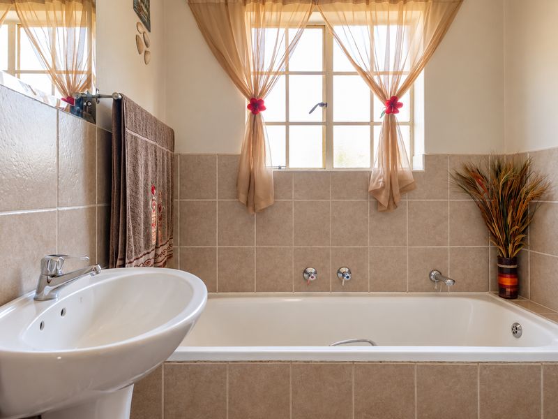 A functional bathroom featuring a pedestal basin and a built-in bathtub with neutral wall tiling and natural light from a window.
