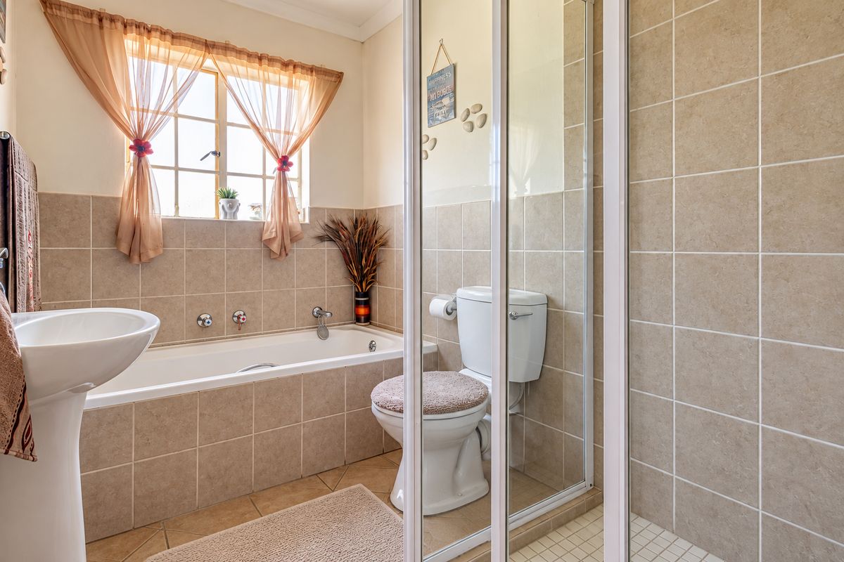 A functional bathroom featuring a pedestal basin, built-in bathtub, and a separate shower enclosure with neutral ceramic wall and floor tiling.