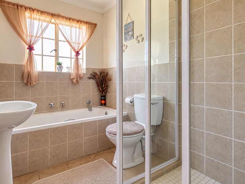 A functional bathroom featuring a pedestal basin, built-in bathtub, and a separate shower enclosure with neutral ceramic wall and floor tiling.