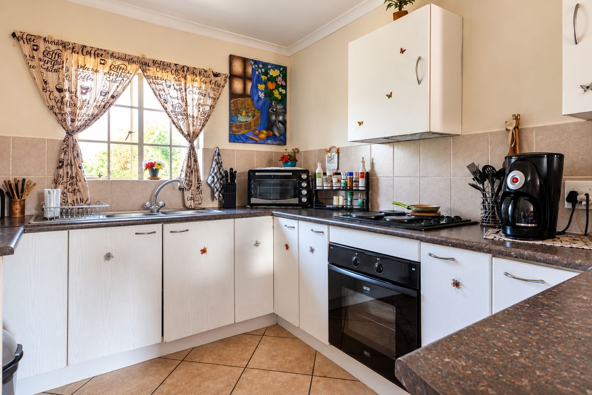 A functional kitchen featuring white cabinetry, dark laminate countertops, a built-in oven with gas hob, and tiled backsplash with ceramic flooring.