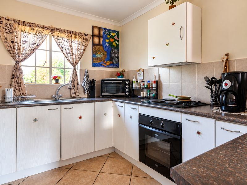 A functional kitchen featuring white cabinetry, dark laminate countertops, a built-in oven with gas hob, and tiled backsplash with ceramic flooring.