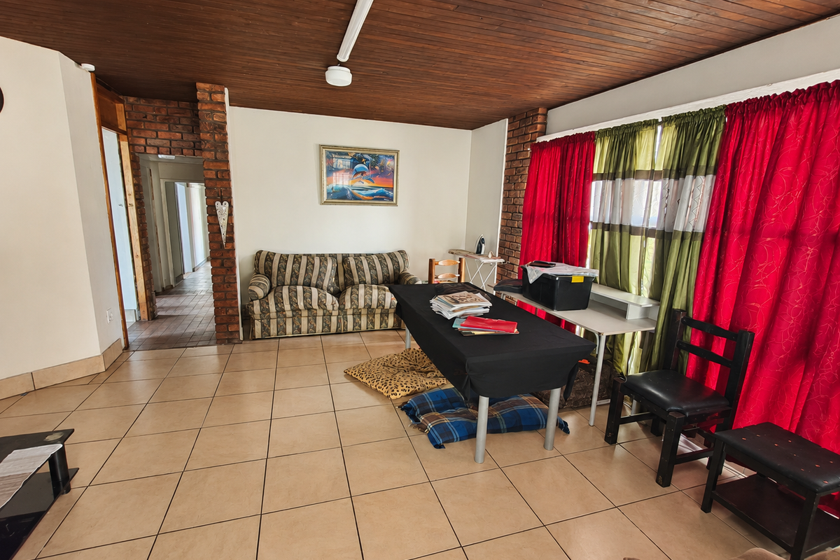 Spacious living area featuring exposed brick pillars, a warm timber tongue and groove ceiling, and neutral ceramic floor tiles throughout.