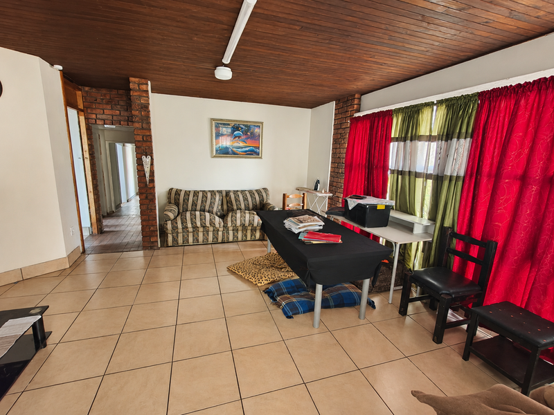 Spacious living area featuring exposed brick pillars, a warm timber tongue and groove ceiling, and neutral ceramic floor tiles throughout.