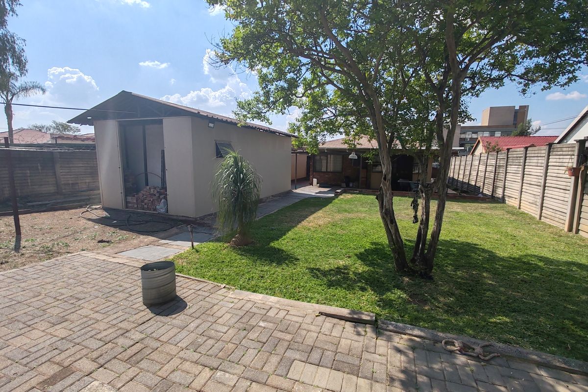 Rear garden area featuring a paved patio, lawn, perimeter walling, and a detached outbuilding structure.