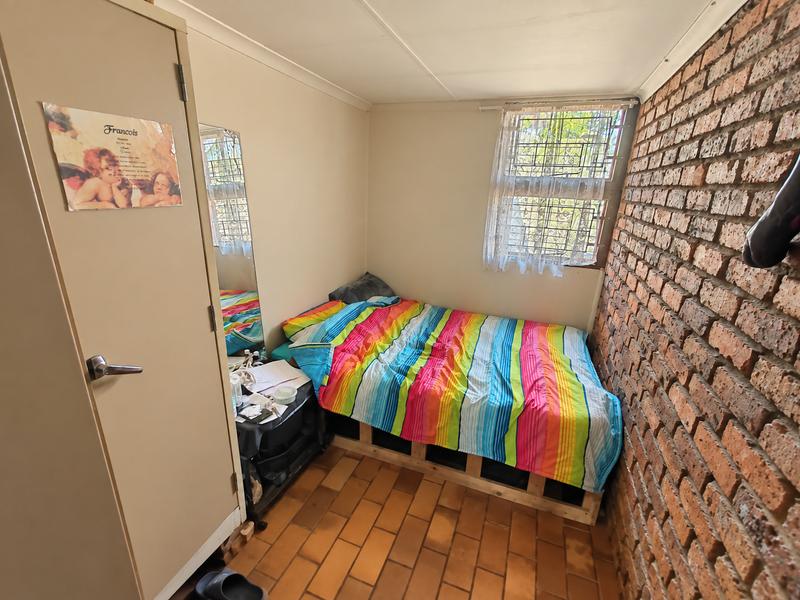 A compact bedroom featuring an exposed brick feature wall, tiled flooring, and a built-in cupboard, offering a functional space with potential for modernization.