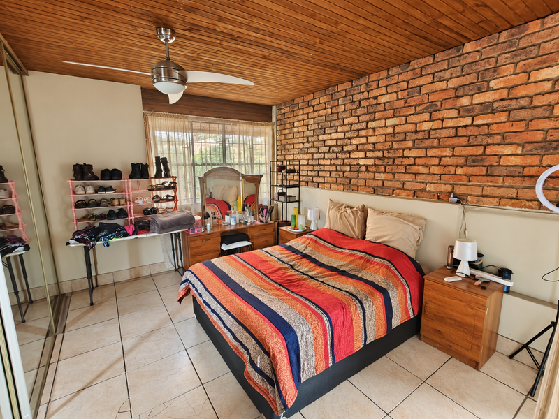 Spacious bedroom featuring a rustic exposed brick feature wall, warm timber ceiling, tiled flooring, and a built-in sliding door wardrobe.