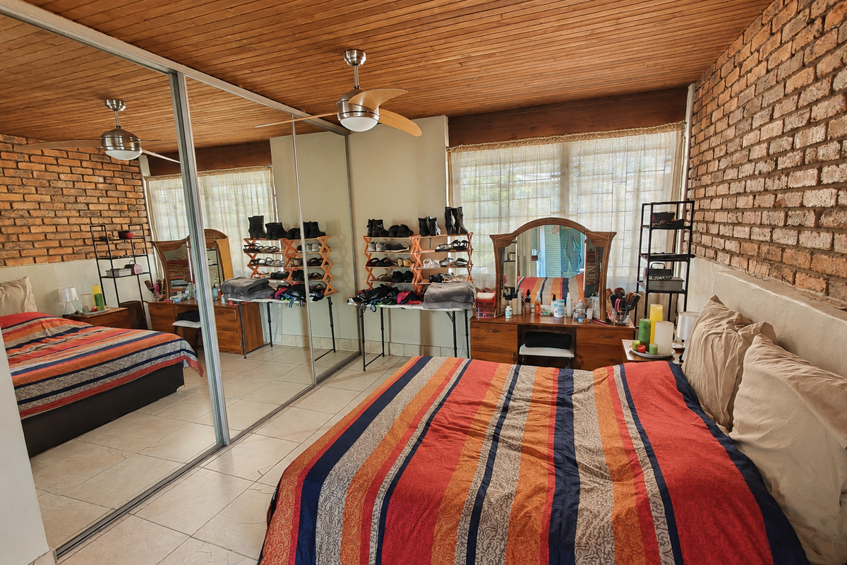 Spacious bedroom featuring exposed brick walls, a timber ceiling, tiled flooring, and large mirrored sliding wardrobes.